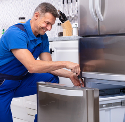 Mature Male Serviceman Repairing Refrigerator With Toolbox In  Kitchen
